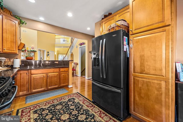 kitchen with brown cabinets, black fridge, a sink, range with gas stovetop, and a peninsula