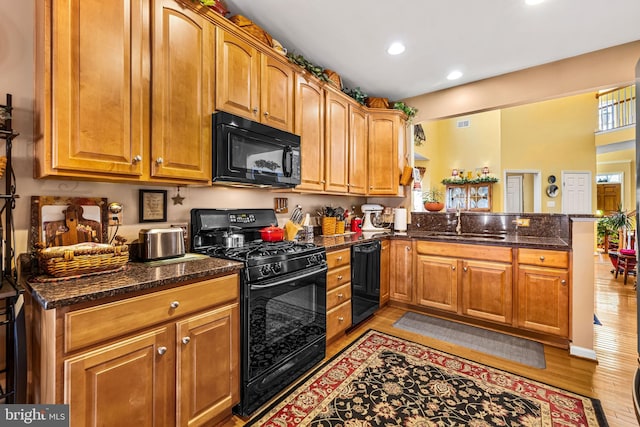 kitchen with light wood-type flooring, a peninsula, a sink, black appliances, and brown cabinets