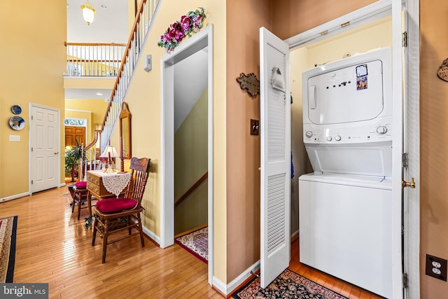 washroom featuring stacked washer / drying machine, wood-type flooring, baseboards, and laundry area