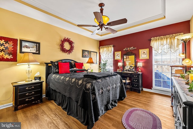 bedroom with baseboards, a raised ceiling, wood finished floors, and ornamental molding