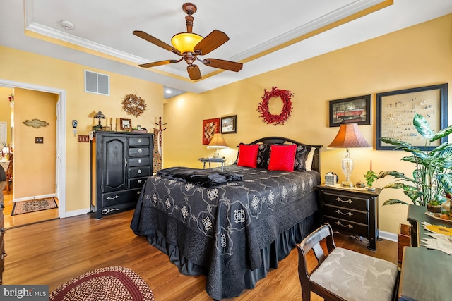 bedroom with visible vents, baseboards, a tray ceiling, ornamental molding, and wood finished floors