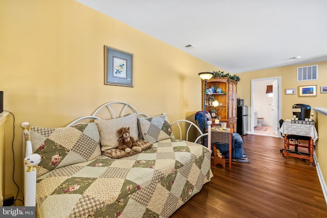 bedroom featuring baseboards, wood finished floors, visible vents, and connected bathroom