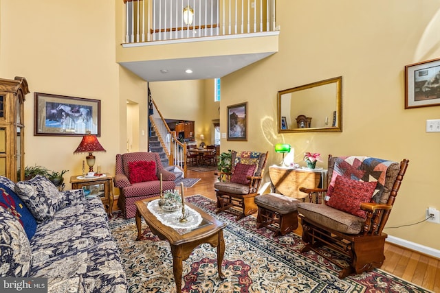 living area with a high ceiling, hardwood / wood-style flooring, stairway, and baseboards