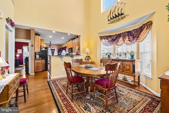 dining room with a high ceiling, plenty of natural light, light wood-style floors, and baseboards