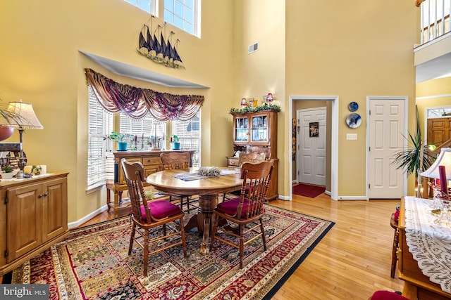 dining area featuring light wood-type flooring, baseboards, a high ceiling, and visible vents