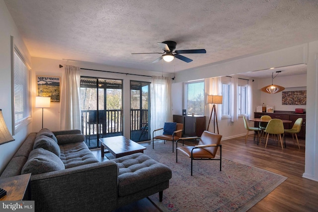 living area featuring a textured ceiling, wood finished floors, a ceiling fan, and baseboards