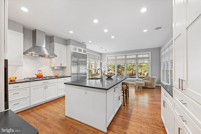 kitchen with wall chimney range hood, tasteful backsplash, dark countertops, appliances with stainless steel finishes, and light wood finished floors