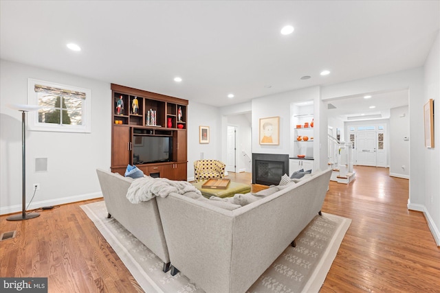 living room with a glass covered fireplace, light wood-style flooring, recessed lighting, and baseboards