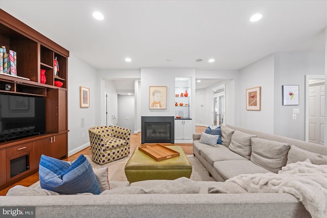 living area featuring light wood finished floors, a glass covered fireplace, recessed lighting, and baseboards