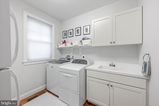 washroom featuring washing machine and clothes dryer, visible vents, baseboards, cabinet space, and a sink