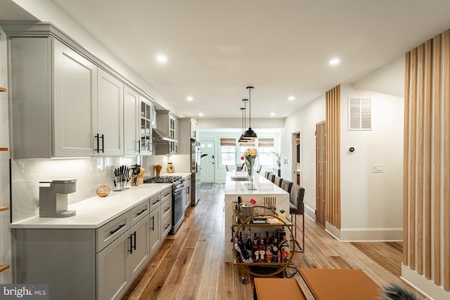 kitchen featuring visible vents, an island with sink, refrigerator, light wood-style floors, and gas stove