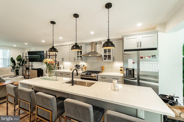 kitchen with a center island with sink, stainless steel appliances, wall chimney range hood, a kitchen bar, and a sink