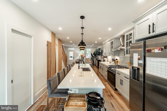 kitchen with a sink, appliances with stainless steel finishes, decorative backsplash, wall chimney exhaust hood, and light wood finished floors