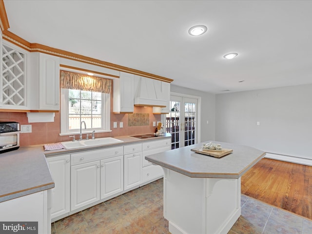 kitchen with tasteful backsplash, a center island, light countertops, white cabinetry, and a sink