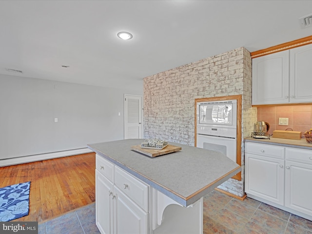 kitchen with oven, white cabinets, baseboard heating, backsplash, and built in microwave