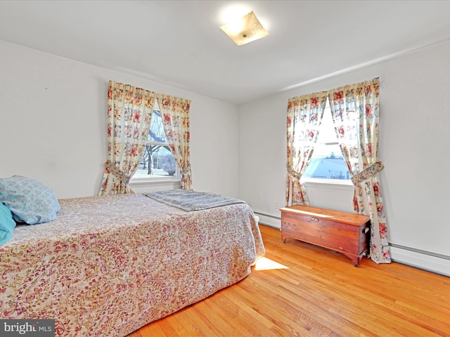 bedroom with a baseboard heating unit, multiple windows, and light wood-style floors