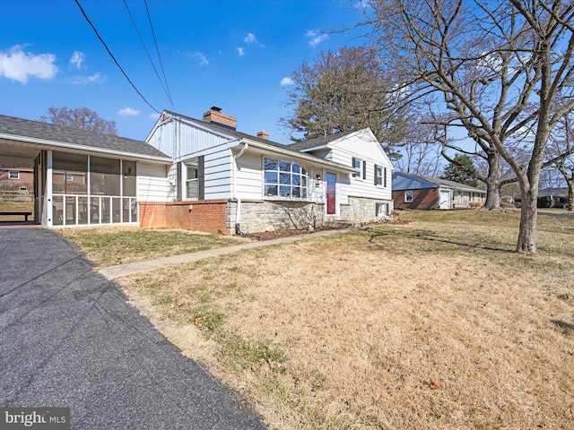 view of front of house with brick siding, a sunroom, stone siding, a front lawn, and a chimney