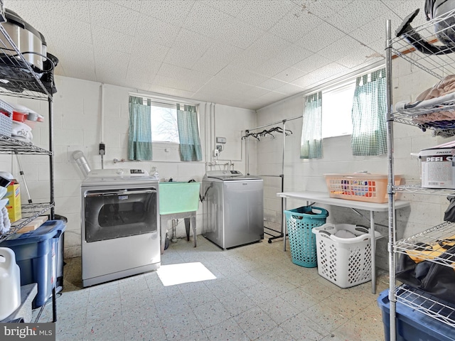 clothes washing area featuring concrete block wall, laundry area, washing machine and dryer, and tile patterned floors