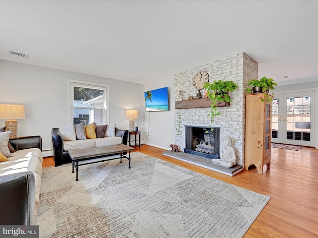 living room featuring a brick fireplace, visible vents, baseboard heating, and wood finished floors