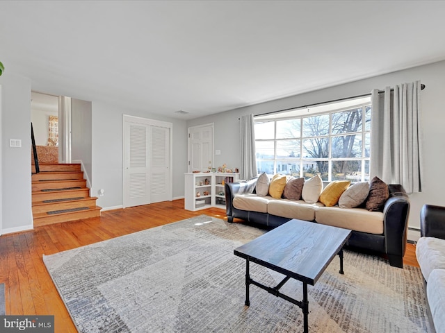 living area featuring a baseboard radiator, wood finished floors, visible vents, baseboards, and stairway