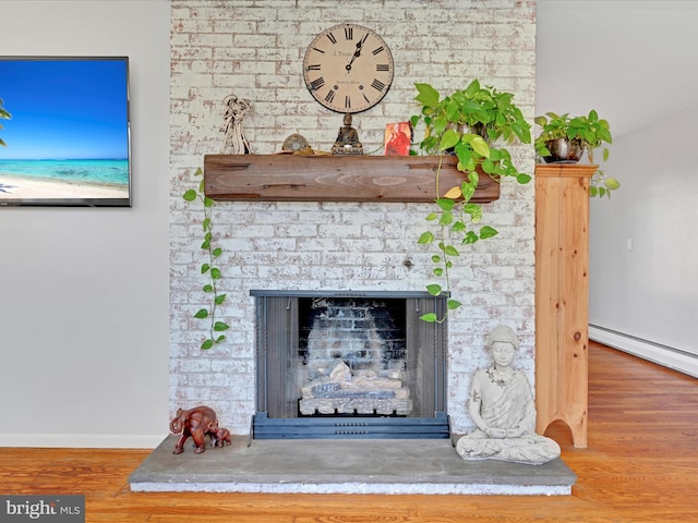 room details featuring a baseboard radiator, baseboards, a fireplace with raised hearth, and wood finished floors