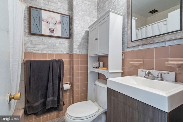 bathroom with tile walls, curtained shower, toilet, wainscoting, and tile patterned floors