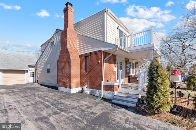 view of side of home featuring a balcony, a chimney, an outdoor structure, and brick siding