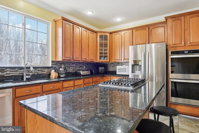 kitchen with a center island, backsplash, dark stone counters, a sink, and appliances with stainless steel finishes