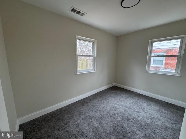 empty room with dark colored carpet, visible vents, and baseboards