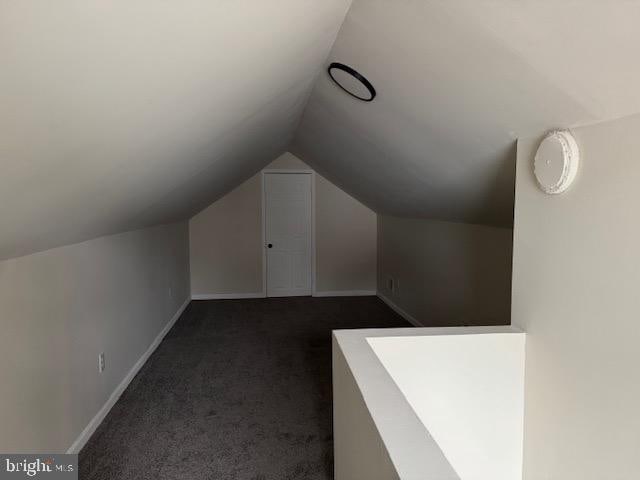 additional living space with lofted ceiling, dark carpet, and baseboards