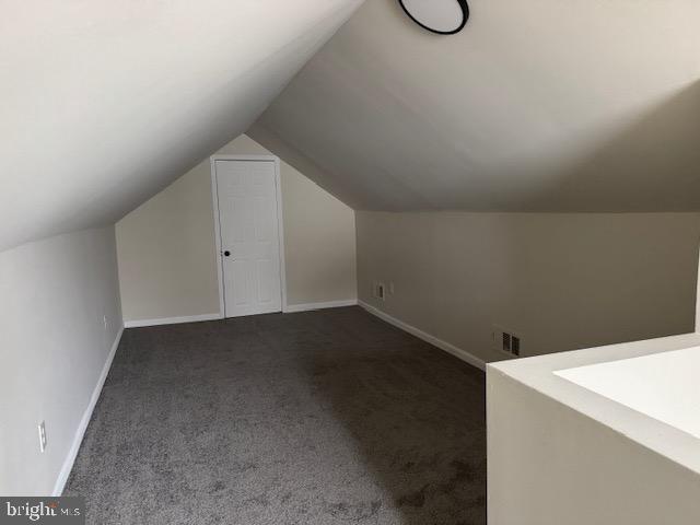 bonus room featuring vaulted ceiling, visible vents, dark carpet, and baseboards