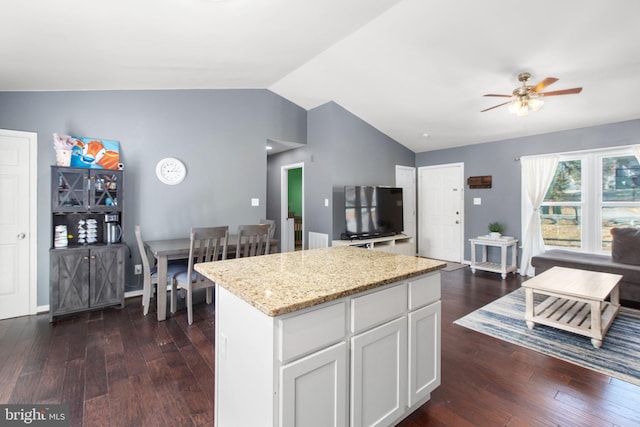 kitchen featuring a kitchen island, lofted ceiling, light stone counters, dark wood-style floors, and white cabinets