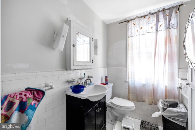 bathroom featuring a wainscoted wall, toilet, tile walls, tile patterned flooring, and vanity