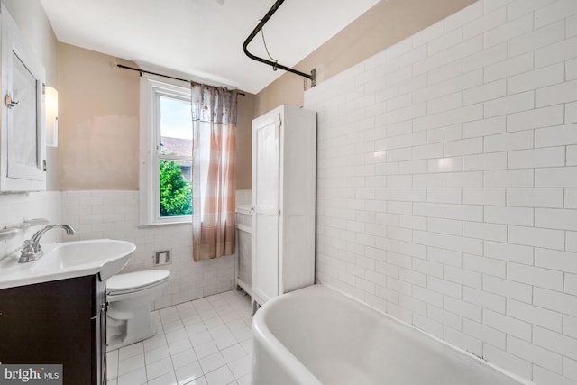 bathroom with tile patterned floors, tile walls, a tub to relax in, vanity, and toilet