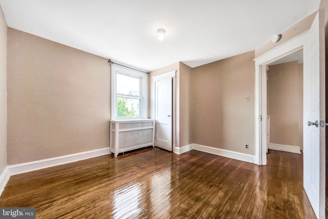 unfurnished bedroom featuring wood-type flooring, baseboards, and radiator heating unit