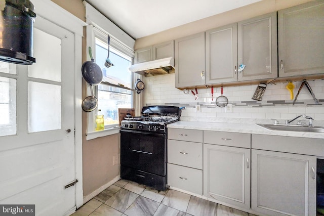 kitchen with black gas range oven, tasteful backsplash, gray cabinetry, under cabinet range hood, and light countertops