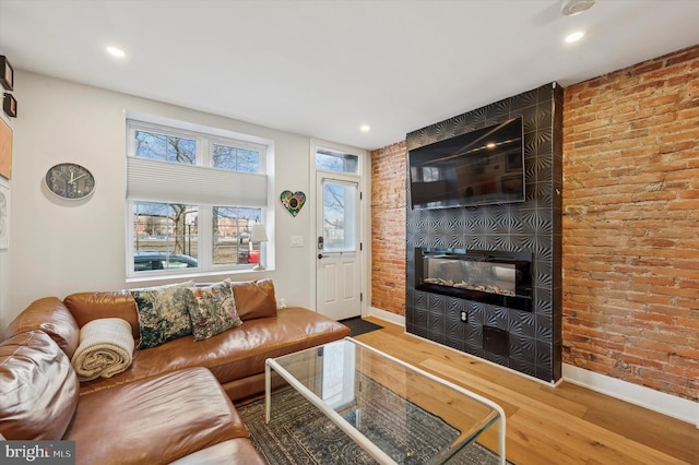 living area featuring a large fireplace, brick wall, baseboards, and wood finished floors