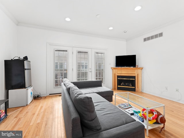 living room featuring visible vents, crown molding, baseboards, a glass covered fireplace, and wood-type flooring