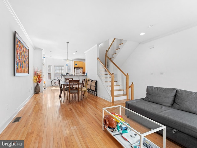 living room featuring visible vents, baseboards, stairway, light wood-type flooring, and ornamental molding