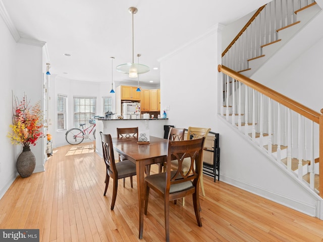 dining space featuring light wood-style flooring, baseboards, ornamental molding, and stairway