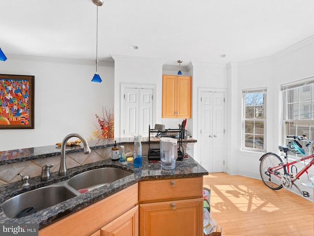 kitchen with crown molding, pendant lighting, dark stone counters, light wood-type flooring, and a sink