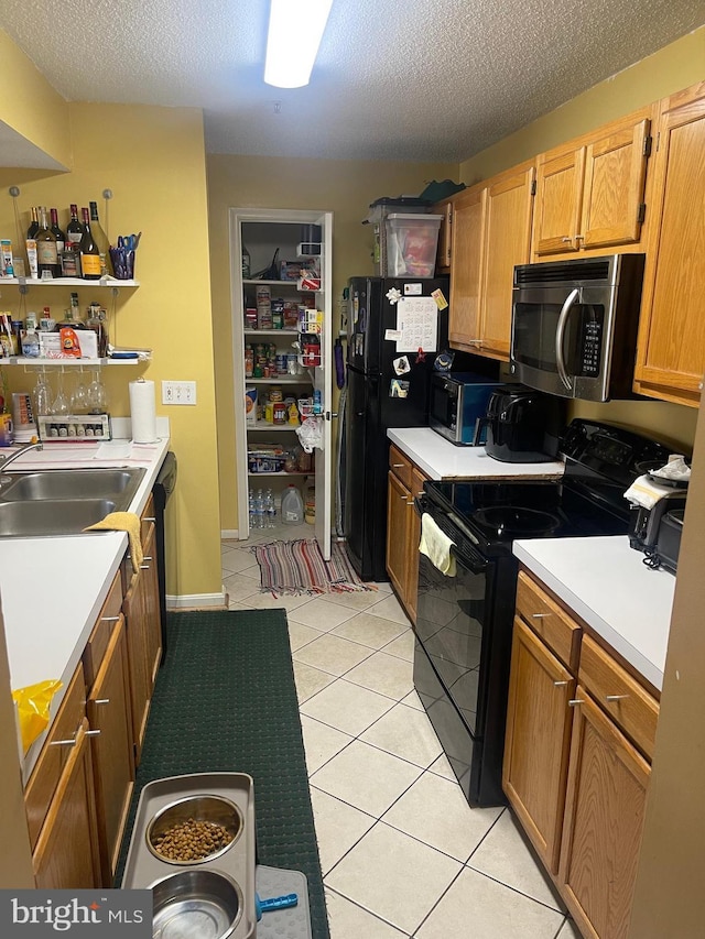 kitchen featuring black appliances, light countertops, light tile patterned floors, a textured ceiling, and a sink