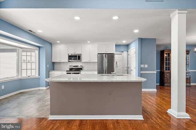 kitchen with decorative columns, a sink, a large island, white cabinets, and appliances with stainless steel finishes