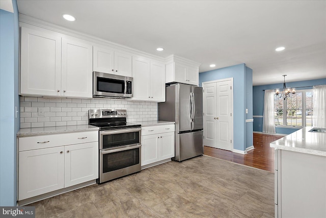 kitchen with light stone countertops, decorative backsplash, appliances with stainless steel finishes, a notable chandelier, and white cabinets