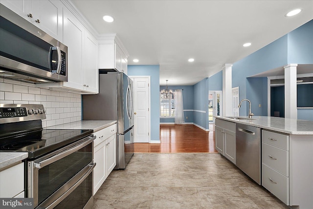 kitchen with a sink, appliances with stainless steel finishes, white cabinetry, a notable chandelier, and tasteful backsplash