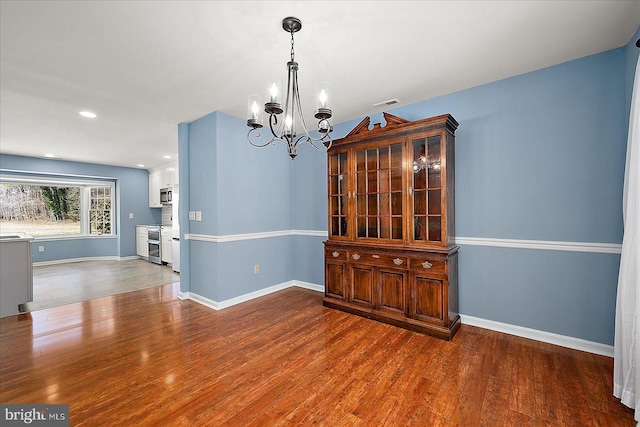 unfurnished dining area featuring recessed lighting, a notable chandelier, wood finished floors, and baseboards