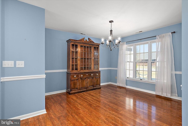 unfurnished room with a chandelier, visible vents, baseboards, and wood finished floors