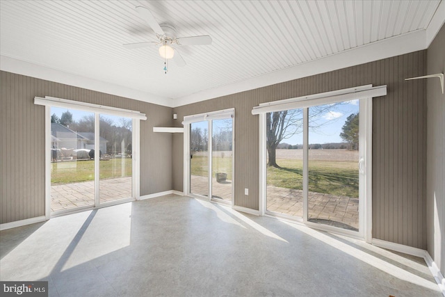 empty room with wooden walls, finished concrete floors, baseboards, and ceiling fan