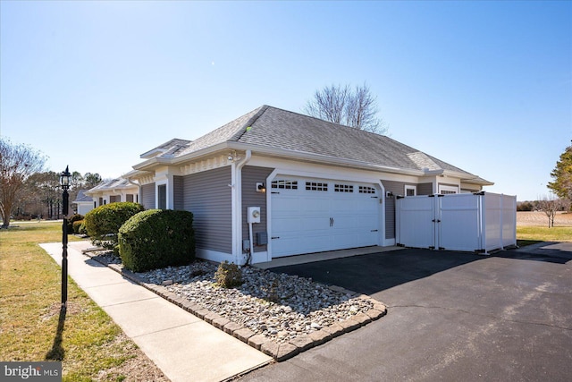 view of side of property with a gate, fence, driveway, roof with shingles, and a garage