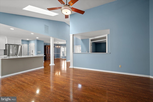 unfurnished living room with baseboards, visible vents, dark wood-type flooring, lofted ceiling with skylight, and ceiling fan with notable chandelier